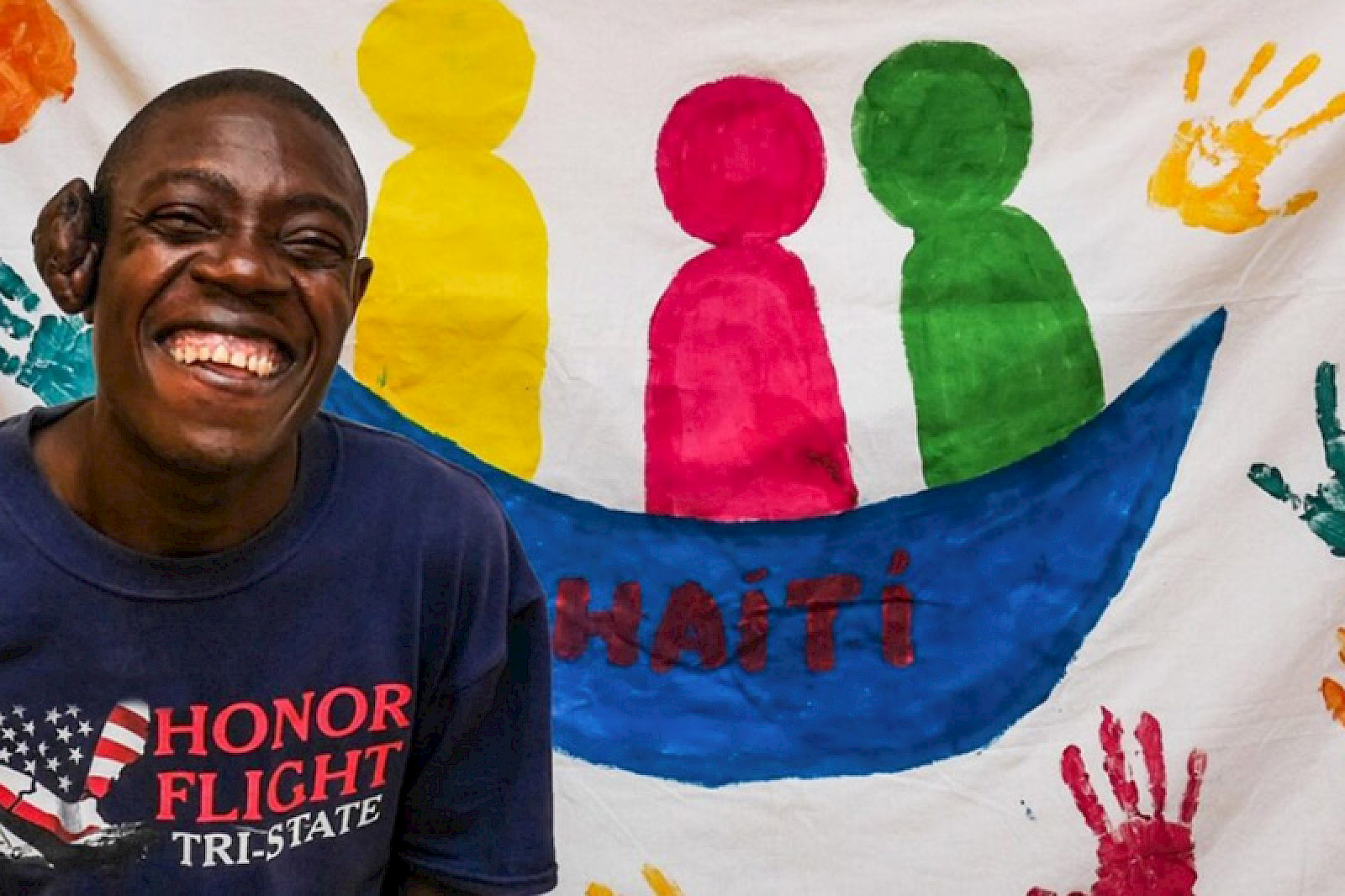 Bild zeigt einen lachenden jungen Mannvor einem Plakat.